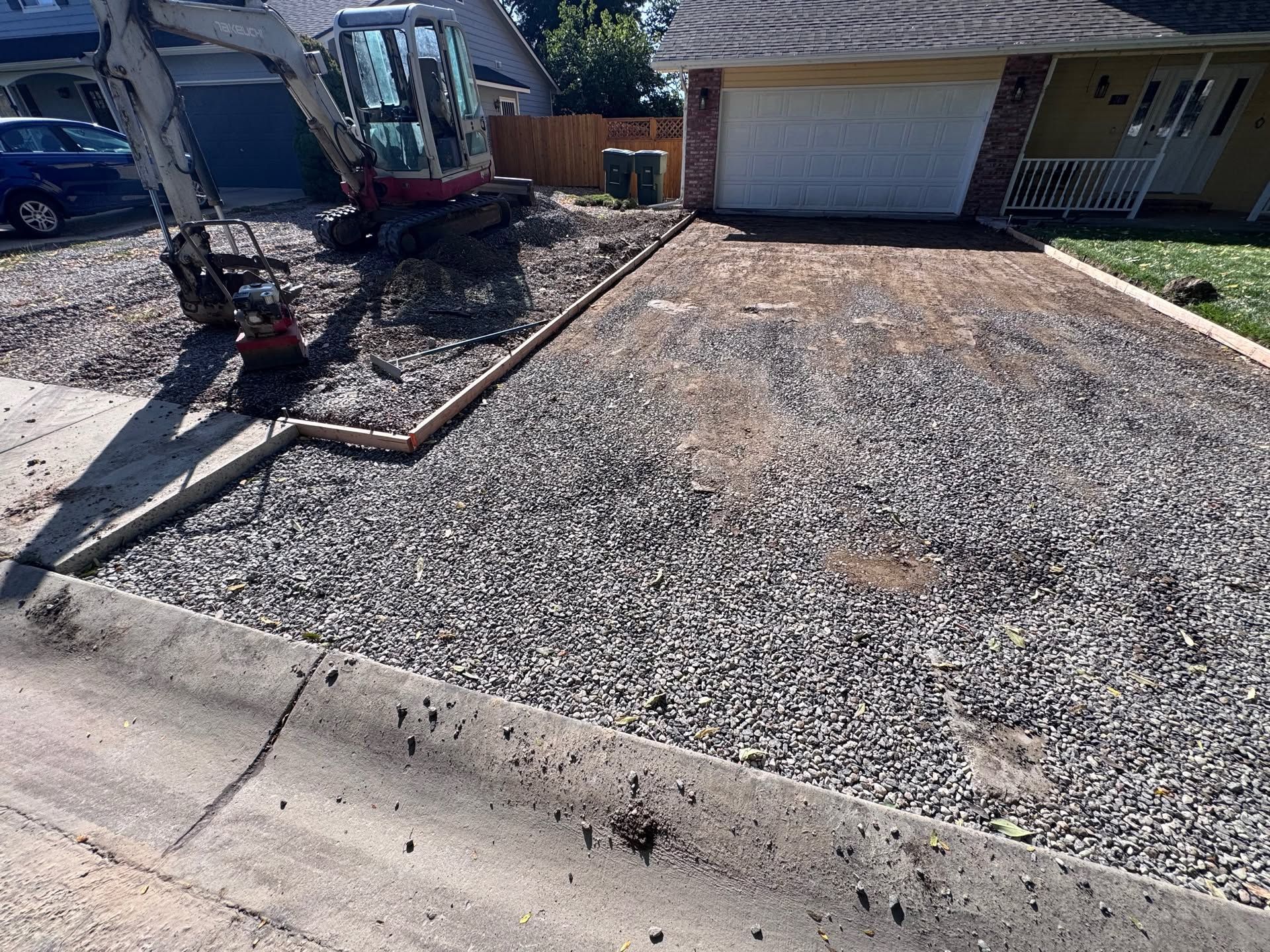 Front yard with fresh gravel driveway leading to a garage, next to a sidewalk and parked truck