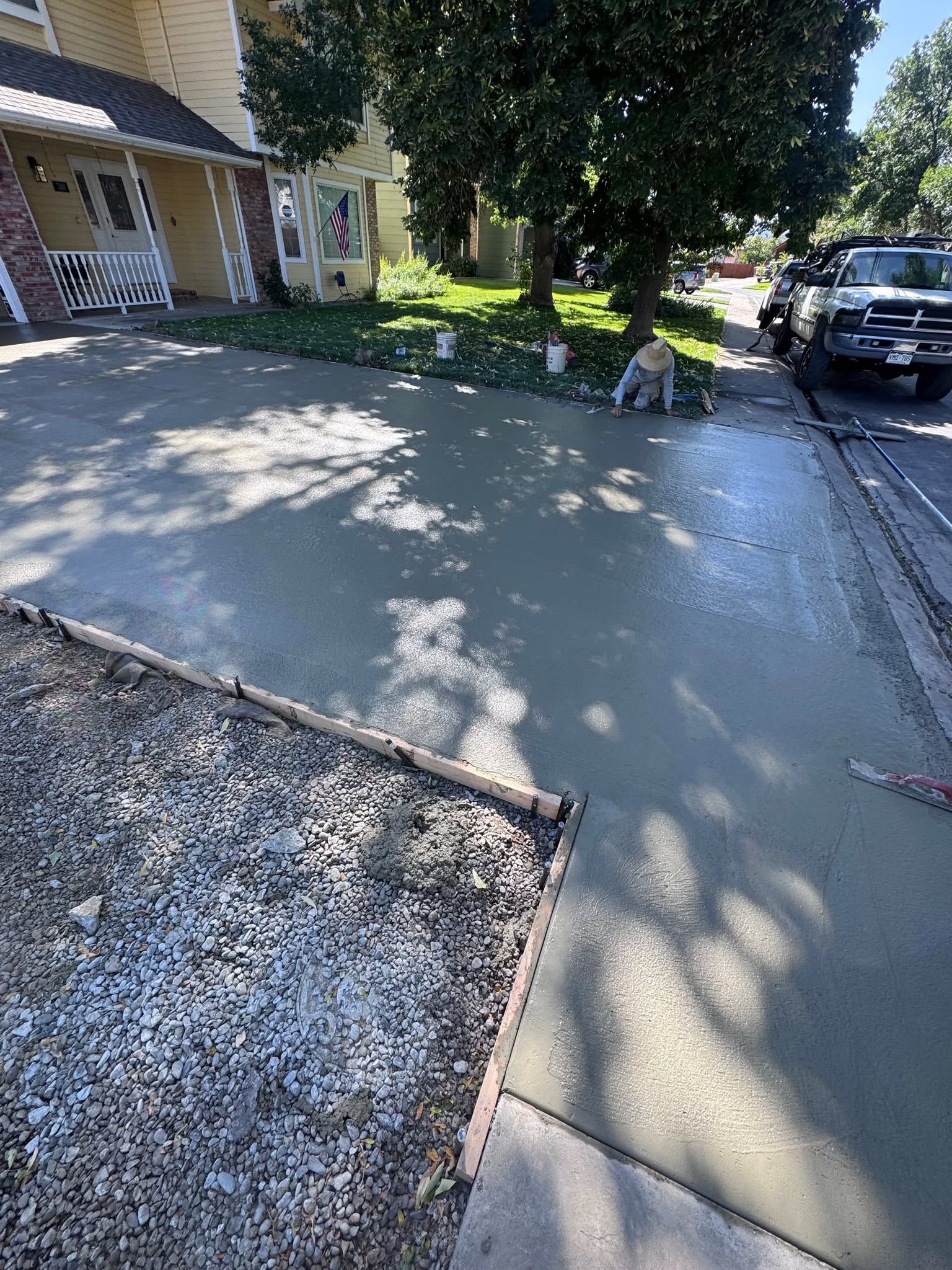 Concrete driveway beside townhouse entrance, with parked truck and shaded sidewalk under a tree.