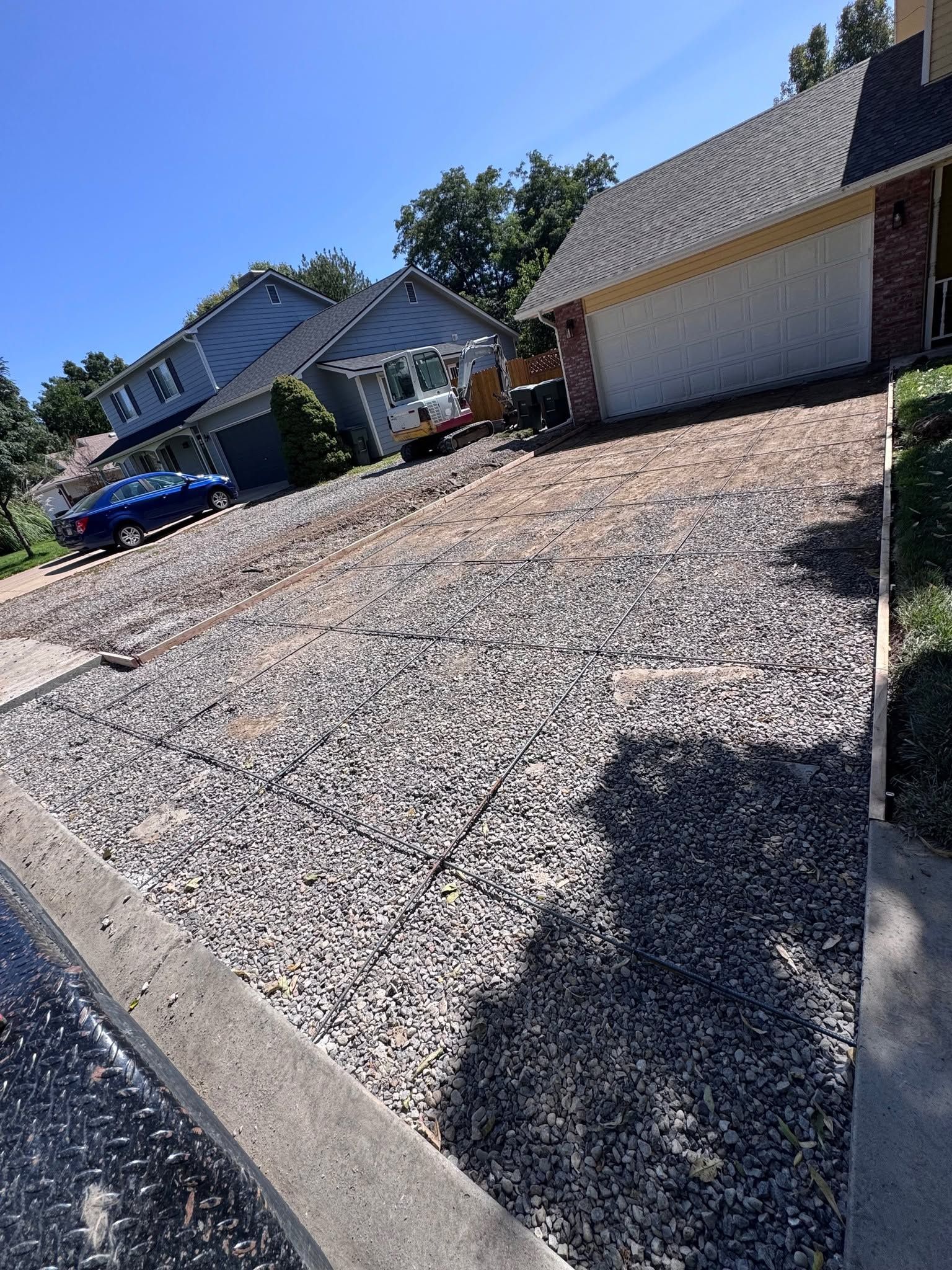 Residential driveway with a parked blue car beside a house and garage on a sunny day