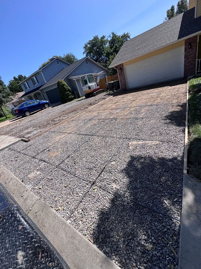 Suburban driveway beside a house and garage, with a blue car parked at the curb.
