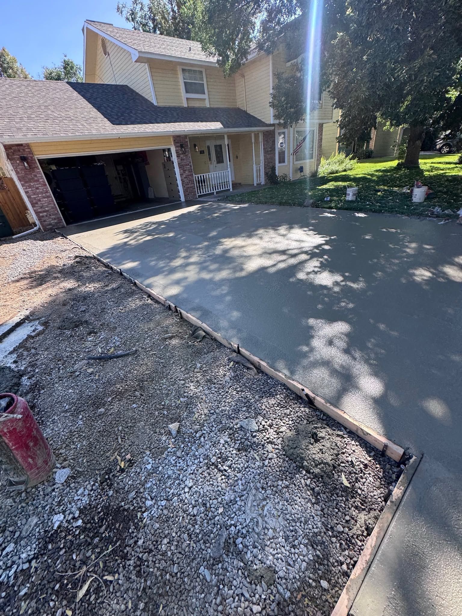 Driveway under construction beside a two-story house, with fresh concrete and gravel border.