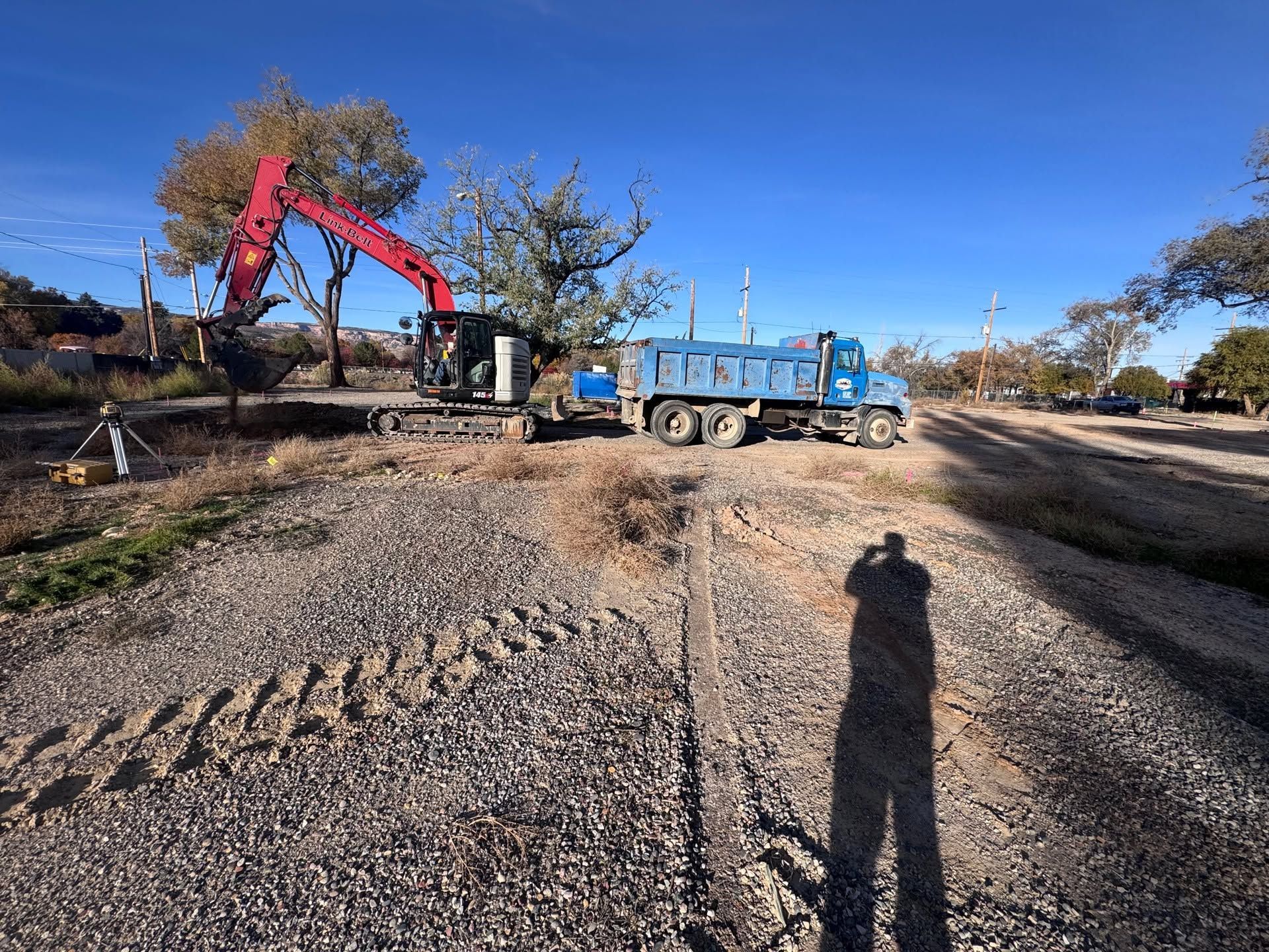 Excavator loading gravel into a blue dump truck at a construction site on a sunny day
