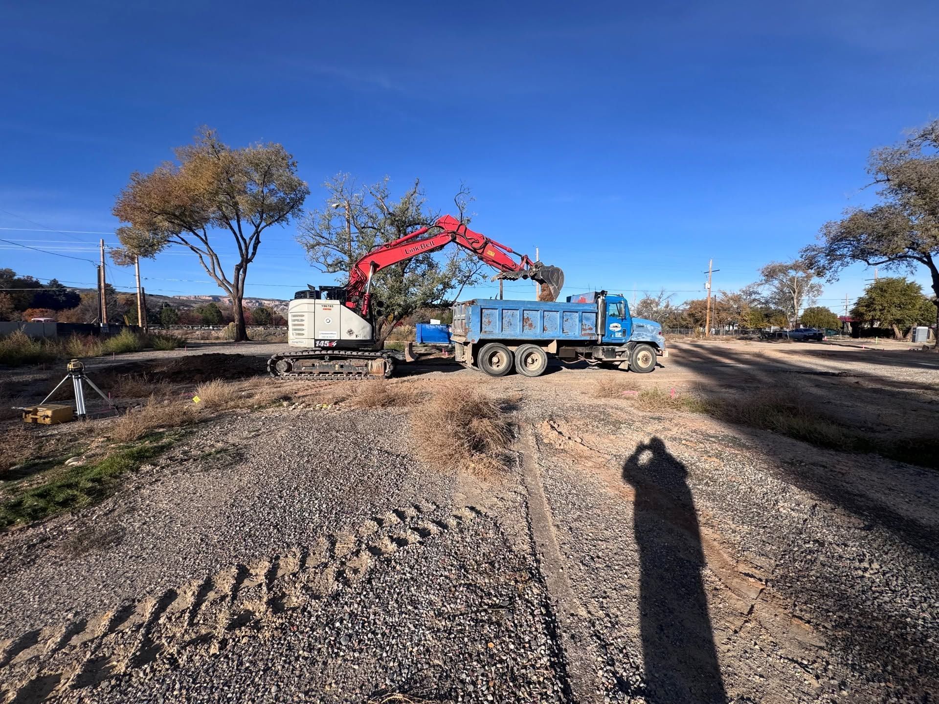 Construction truck and red excavator on a gravel road under a clear blue sky.