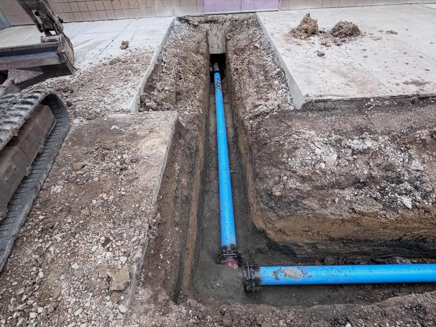 Blue PVC pipes installed in a dirt trench at a construction site