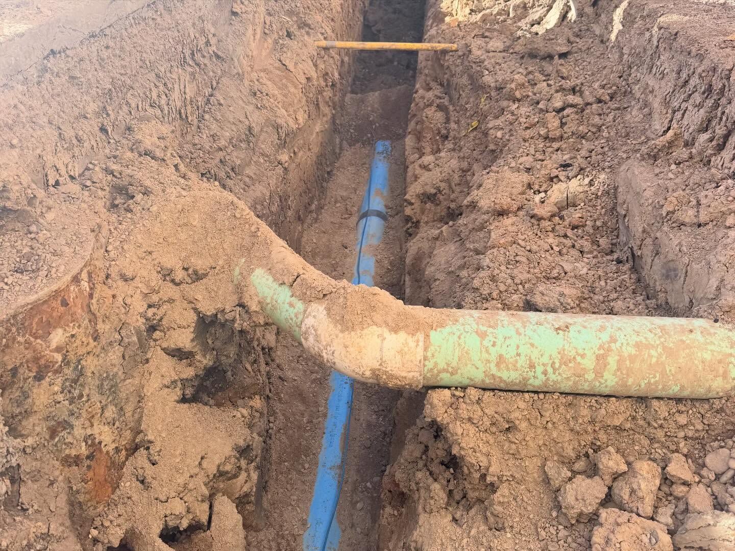 Rusty pipes crossing a dirt trench with a blue pipe visible below