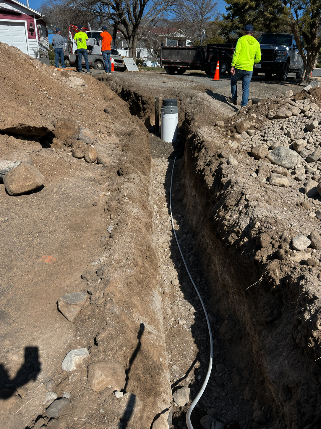 Workers in neon safety gear standing beside a deep trench at a construction site