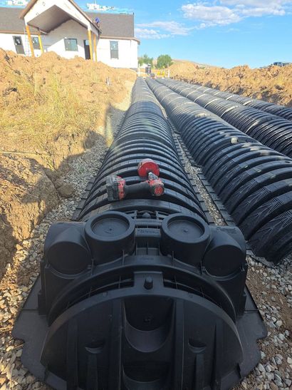 Black plastic pipes laid in a trench beside a house under a blue sky