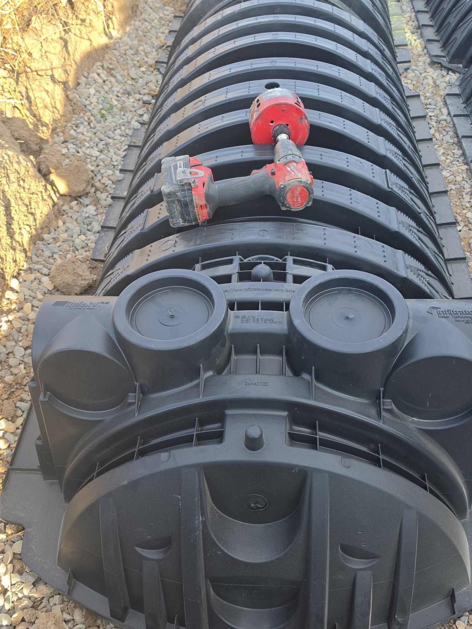 Black cylindrical utility conduit in a trench, with red couplings and capped ends during installation