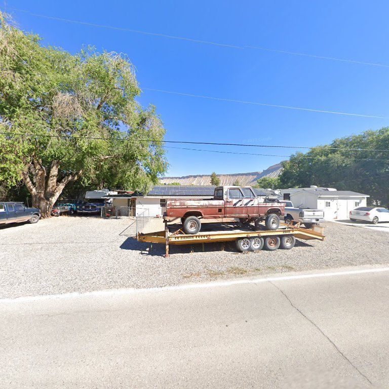 Red vintage pickup on a flatbed trailer parked in a gravel driveway with trees and houses nearby