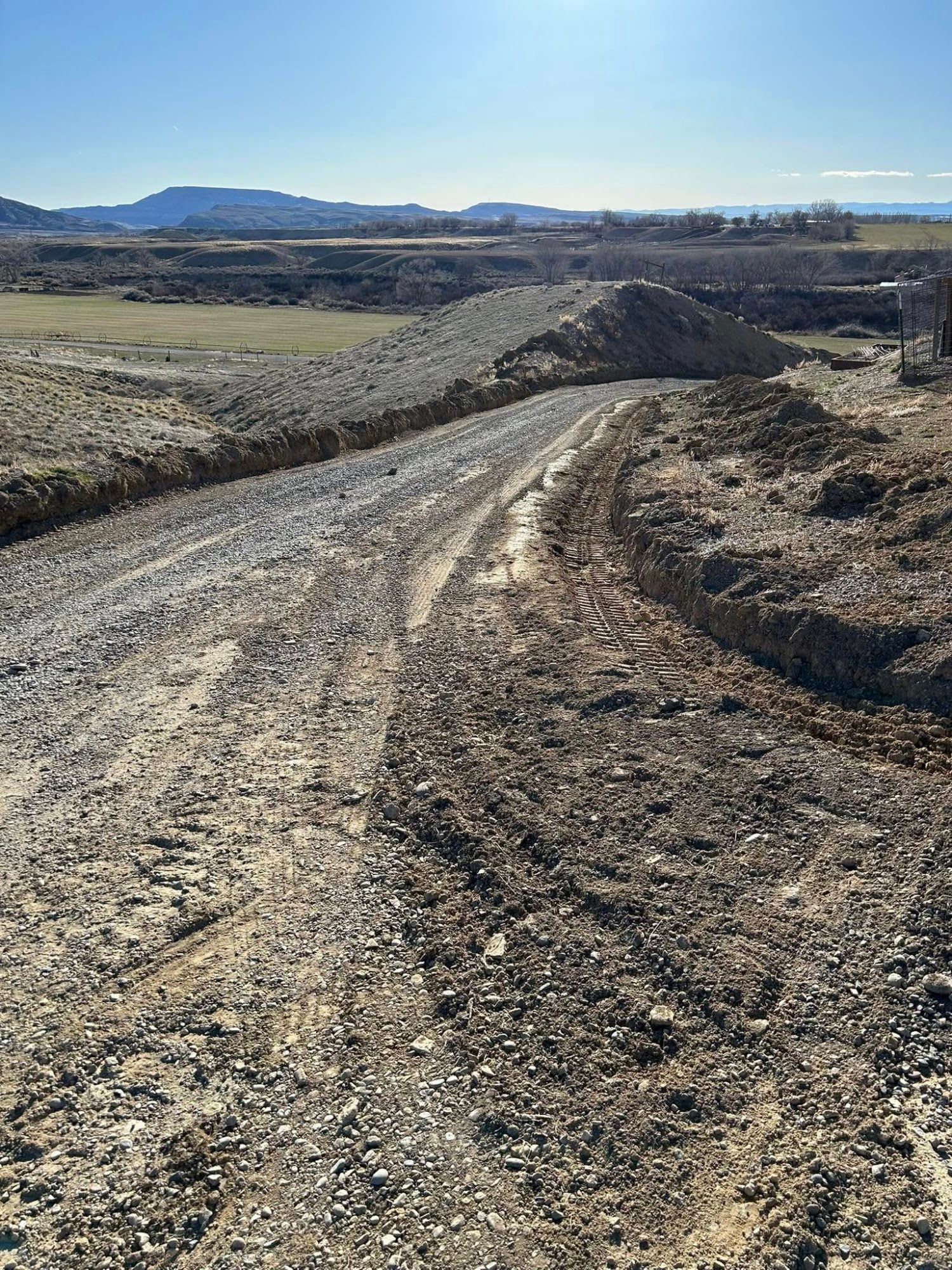 Dirt road curving through a barren rural landscape with hills in the distance