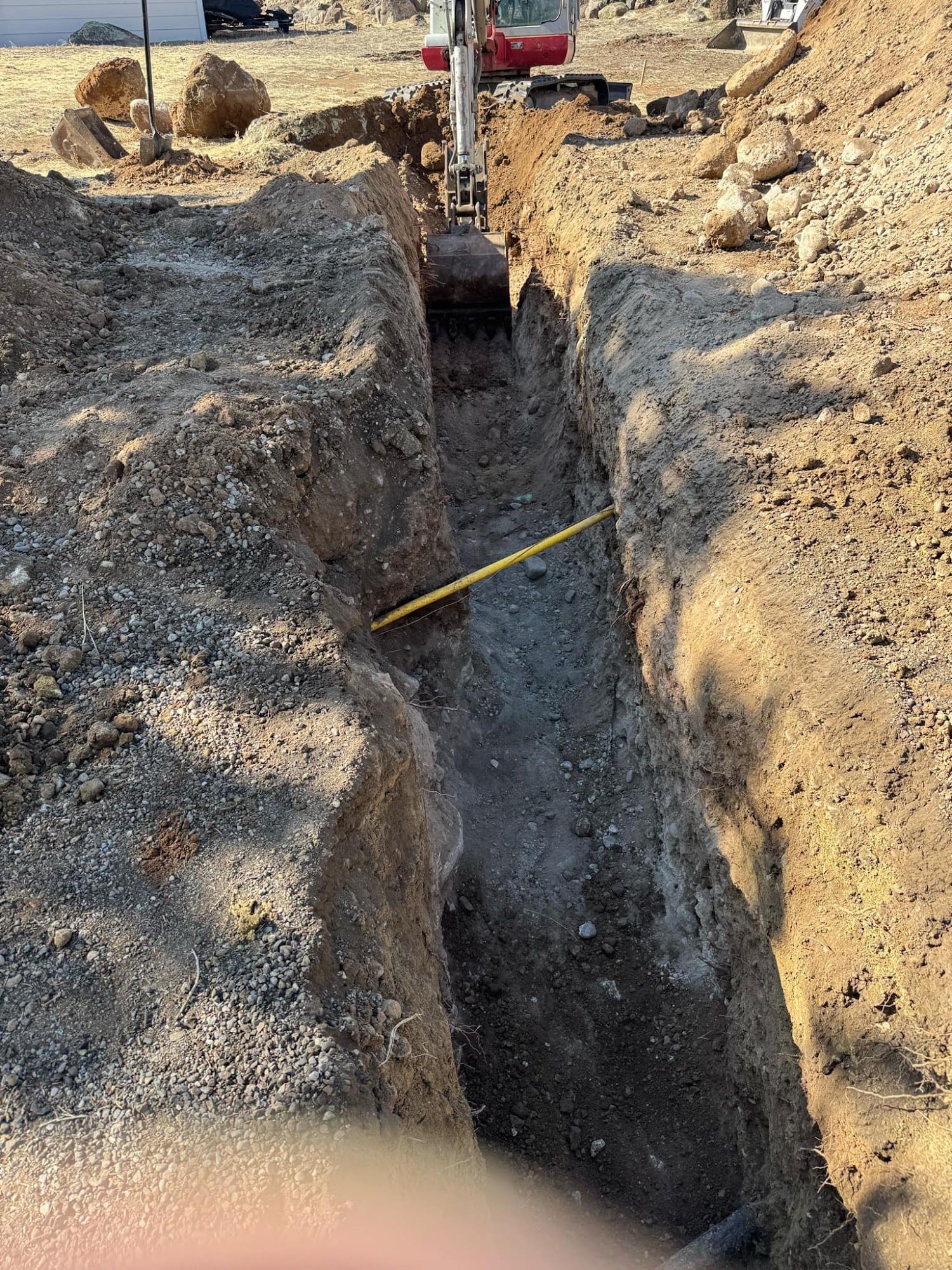 A deep trench cut into rocky soil at a construction site, with a measuring tape stretched across it.