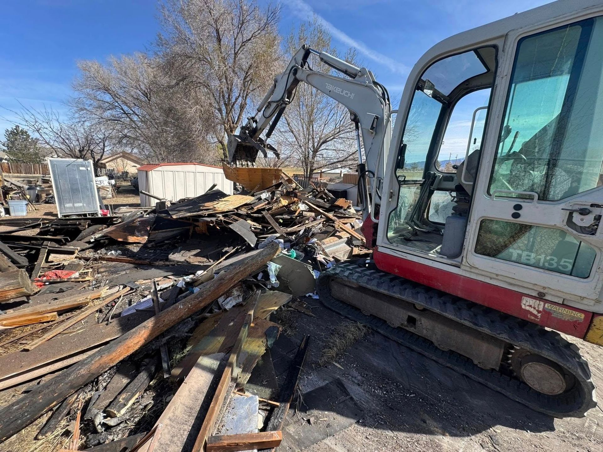 Excavator demolishing debris at a wrecked site under a clear sky
