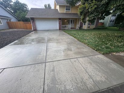 Suburban house with wet concrete driveway, garage, lawn, and trees after rain