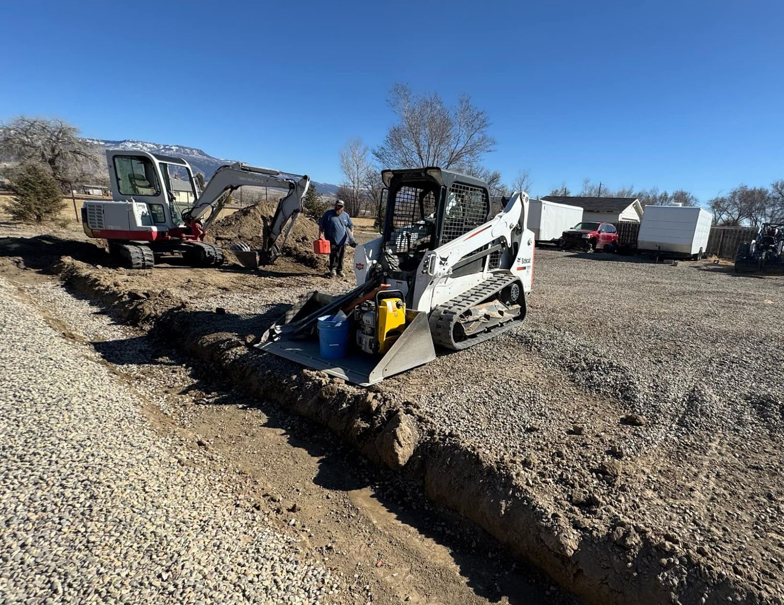 Construction crew operating skid steer in gravel pit beside a dump truck on a sunny day
