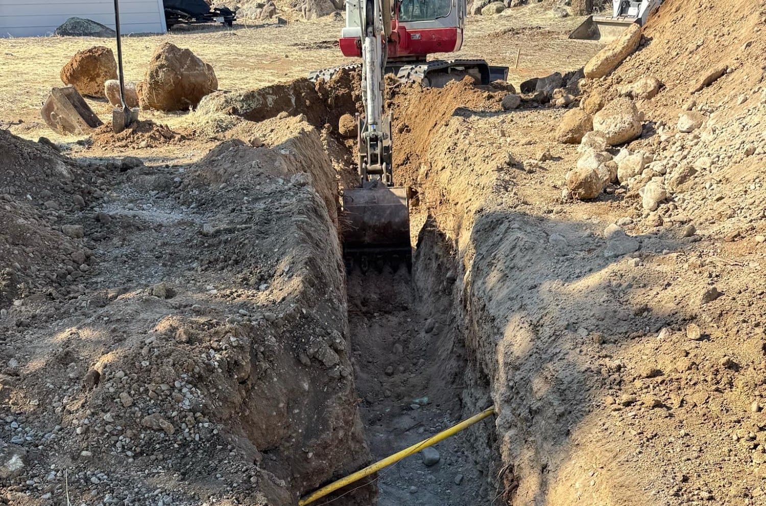 Excavator digging a trench at a construction site beside rocks and dirt piles