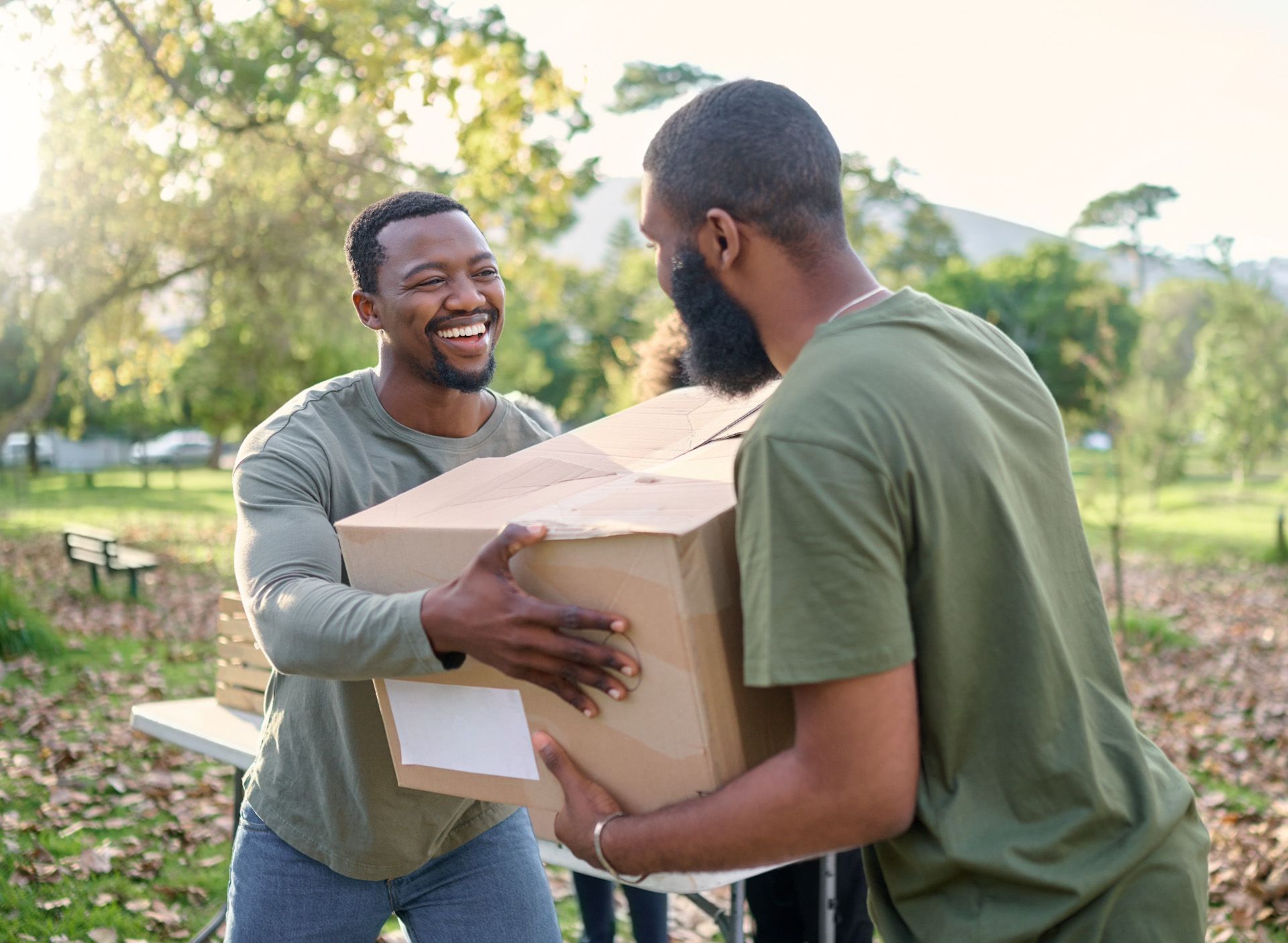 Two men are carrying a cardboard box in a park.