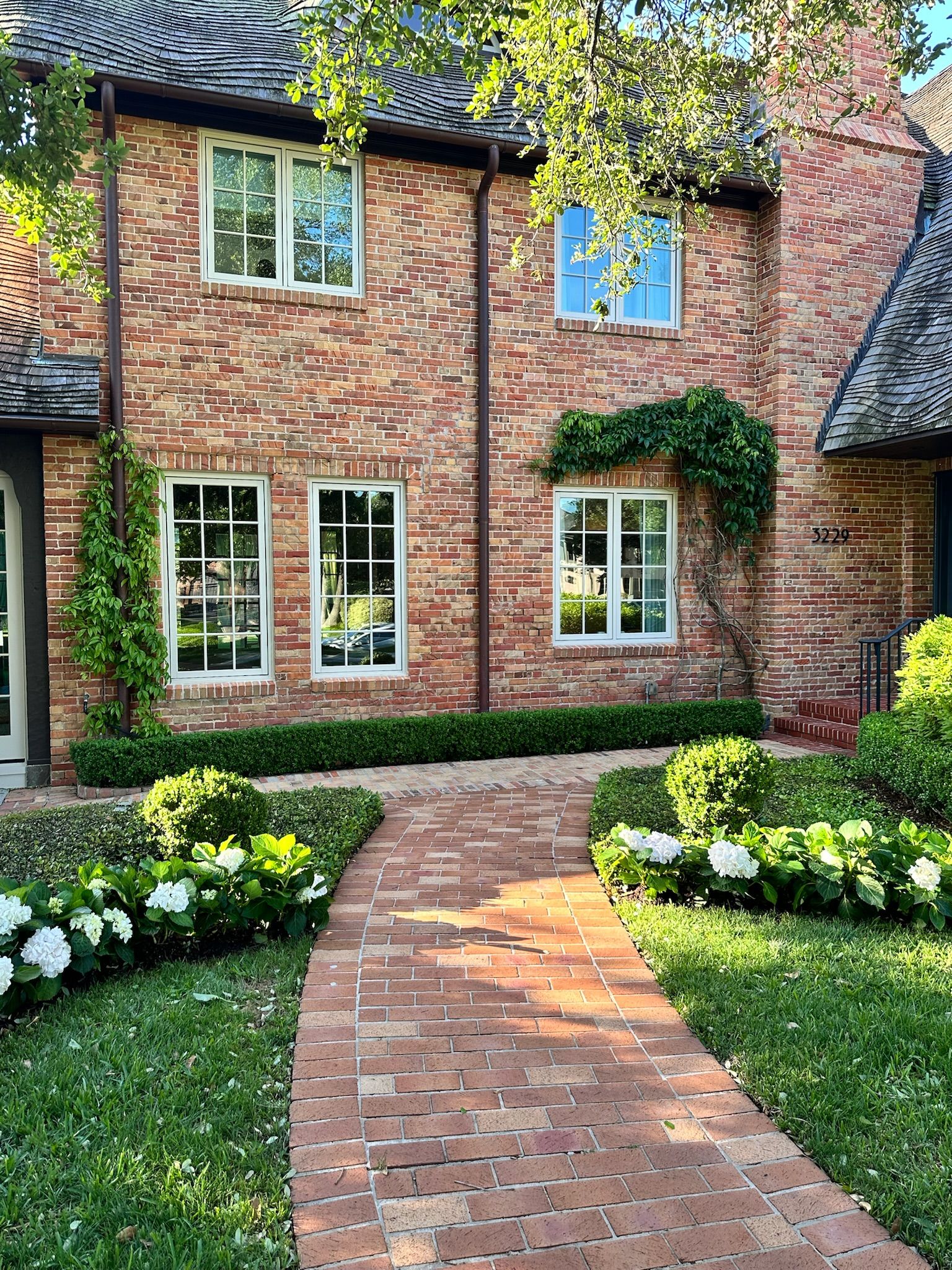 Brick house with white-trimmed windows and a curved brick path through a green garden
