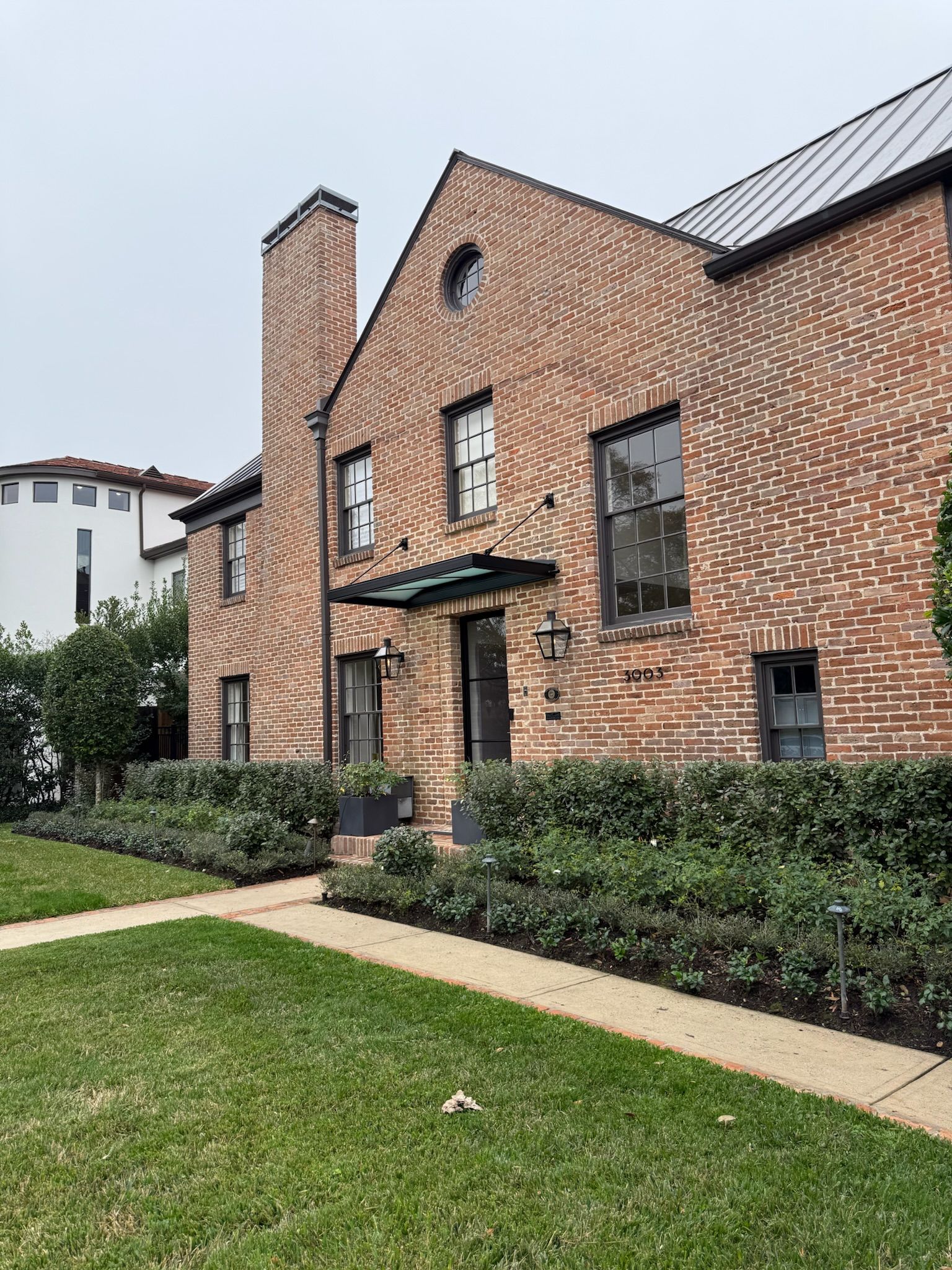 Brick house exterior with front door, chimney, and manicured lawn under a cloudy sky