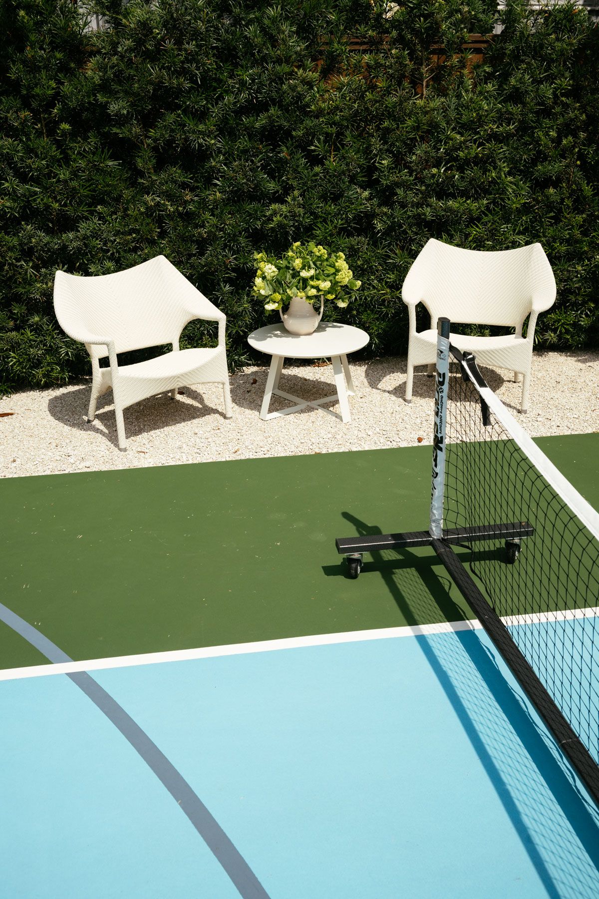 Poolside patio with two white chairs, a small table, and a hedge backdrop beside a swimming pool.