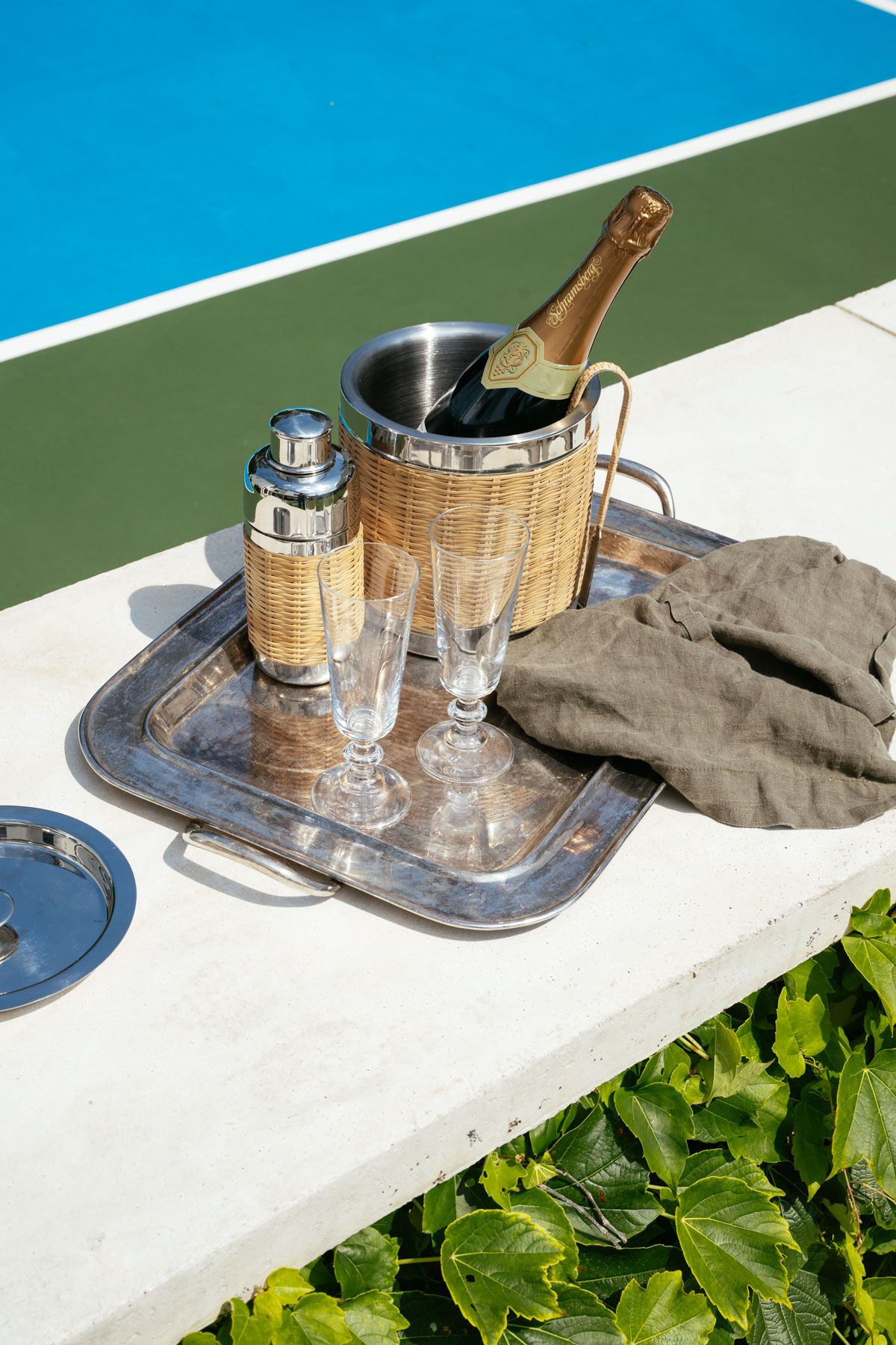 Poolside tray with champagne bottle, glasses, shaker, and towel on a white ledge