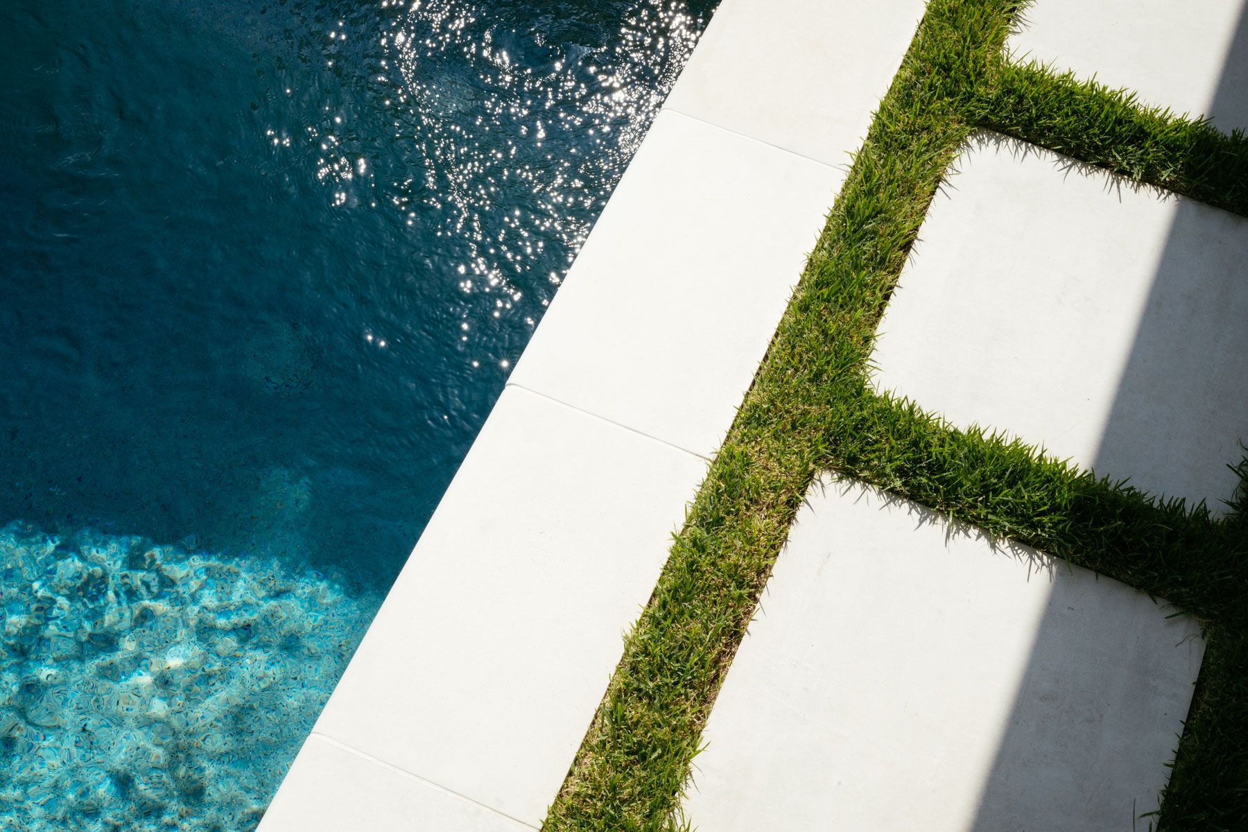Blue swimming pool beside white concrete and green grass-lined stepping paths