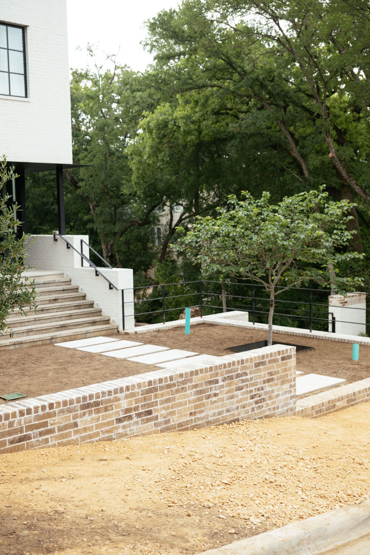 Outdoor walkway beside a white building, with brick planters, steps, and trees on a gravel path.