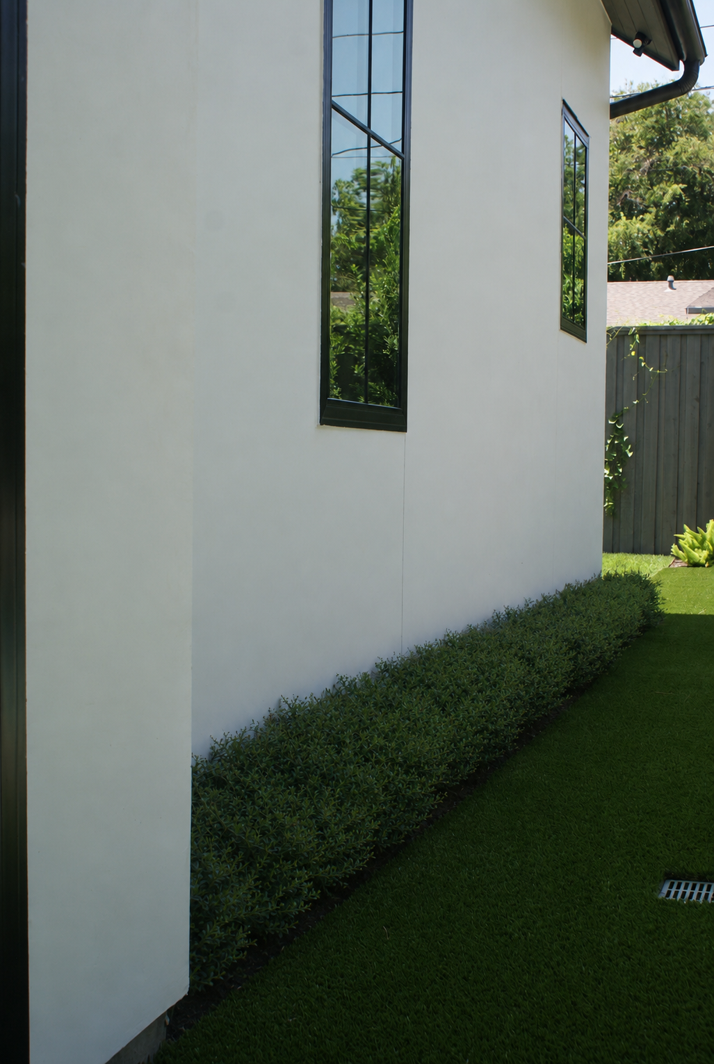 Two people standing on a lawn beside a modern house, chatting in the sun