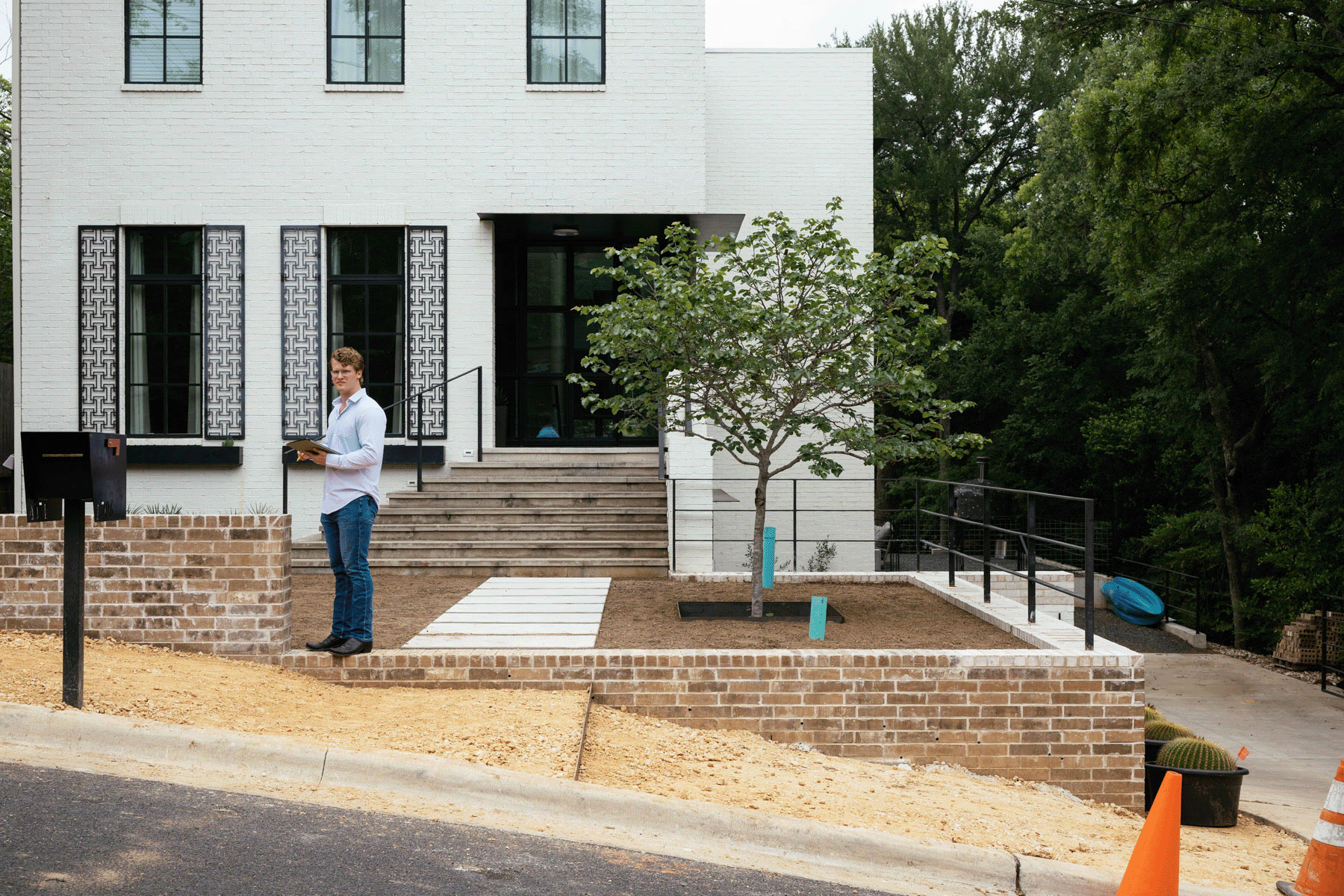 Person standing by a white house with brick steps, ramp, and landscaped front yard