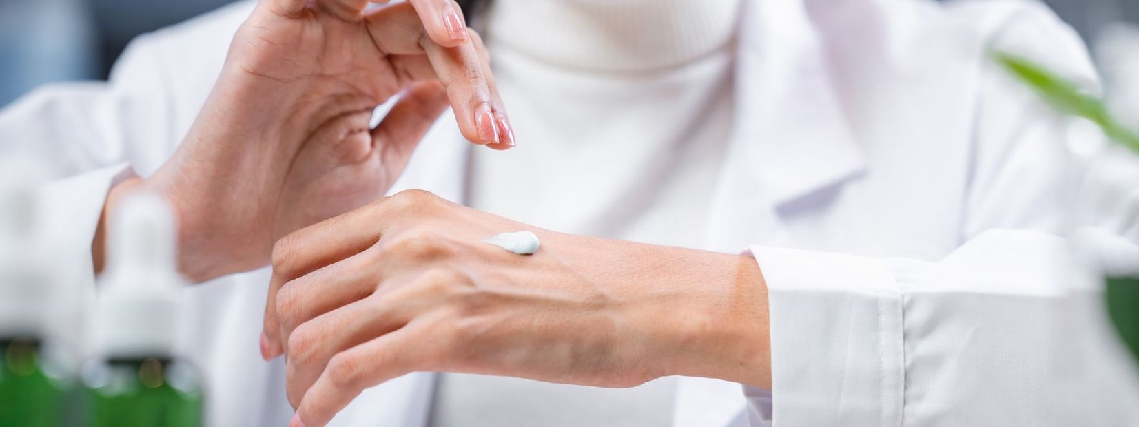 Person applying cream to hand, wearing a white lab coat.