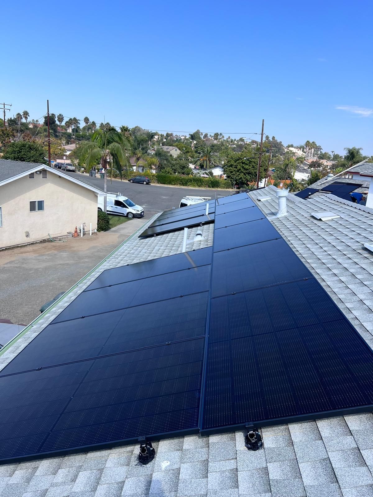 Solar panels installed on a rooftop overlooking a suburban neighborhood under a clear blue sky