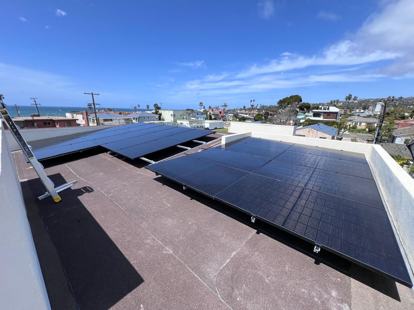 Solar panels mounted on a rooftop under a clear blue sky, overlooking a coastal neighborhood.