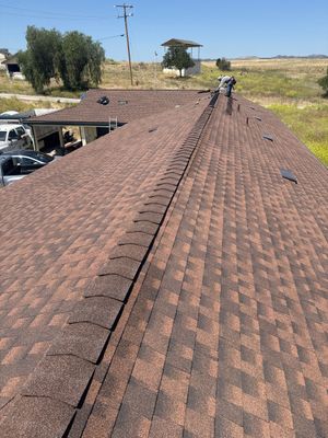 Workers on a brown shingle roof during repairs on a sunny rural property.