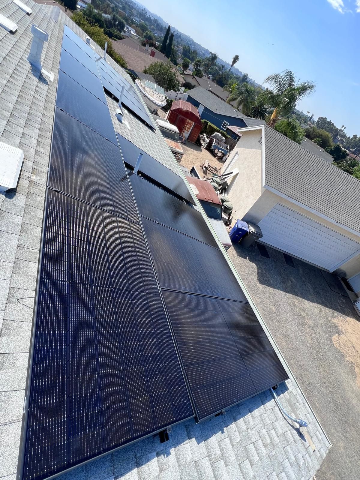 Rooftop solar panels on a house next to a driveway and neighboring homes, viewed at an angle.