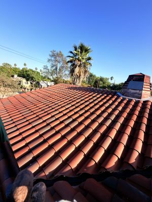 Red terracotta tile roof with a chimney under a clear blue sky, with trees in the background