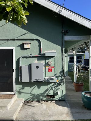 Exterior wall with utility boxes and a door beside a covered walkway, in bright sunlight.