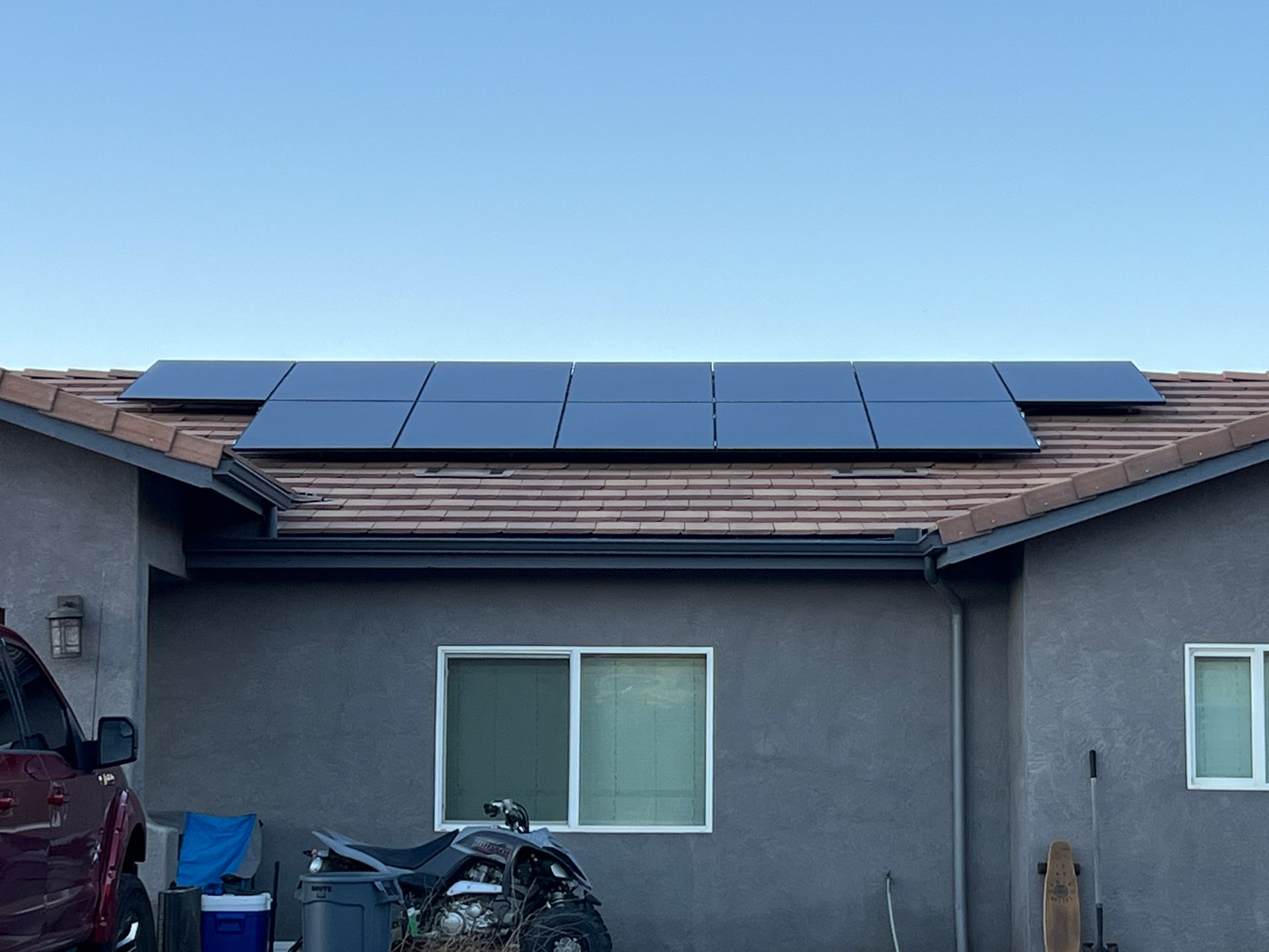Solar panels installed across a gray house roof under a clear blue sky.