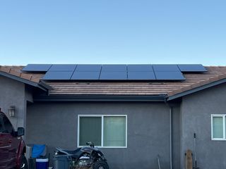Solar panels mounted on a gray house roof under a clear blue sky