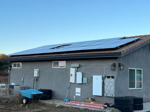 House with rooftop solar panels and utility meters on a gray exterior wall