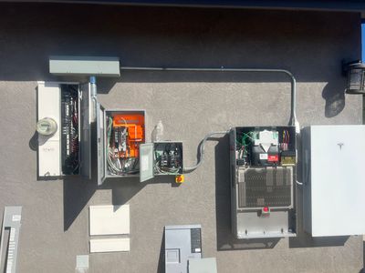 Electrical panels and wiring mounted on a wall, with open breaker boxes and conduit overhead