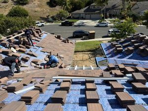 Workers installing blue tarps and brown shingles on a roof in a residential neighborhood