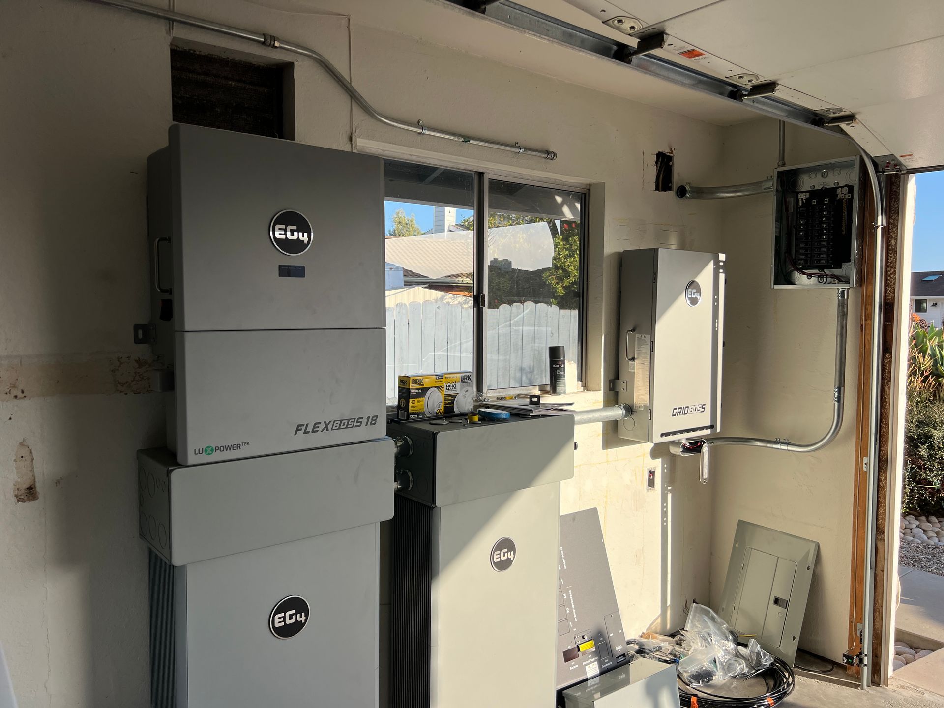 Garage wall with electrical equipment boxes, wiring, and an open doorway to the outdoors