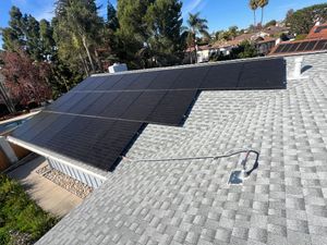 Solar panels on a sloped roof beside gray shingles, with a small tool on the roof under a clear sky.