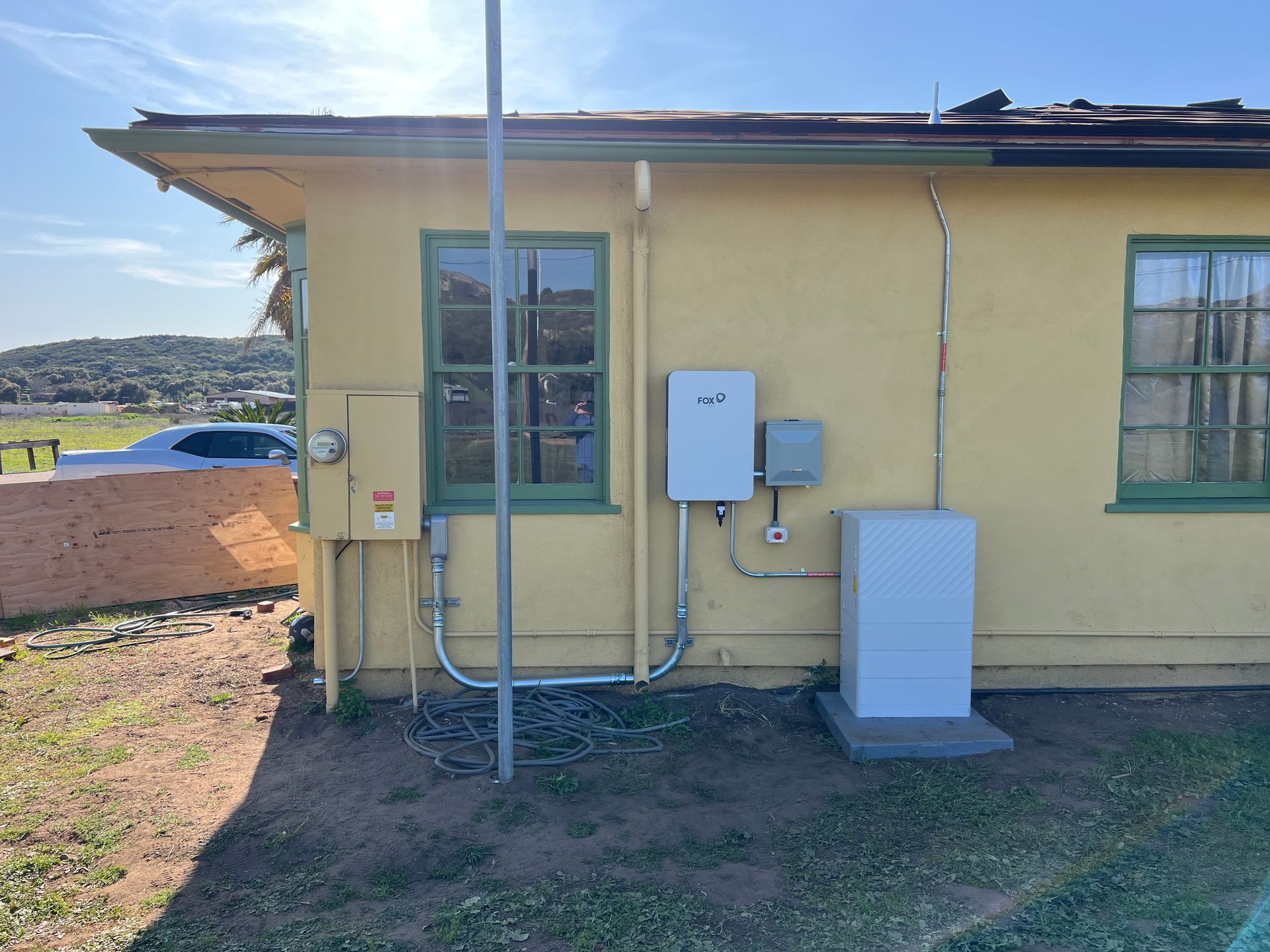 Yellow building exterior with utility meters, pipes, and a blue-trimmed window