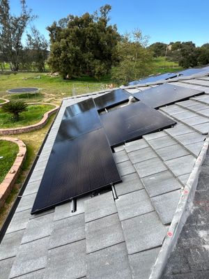 Solar panels installed on a shingled roof beside trees and a green yard.