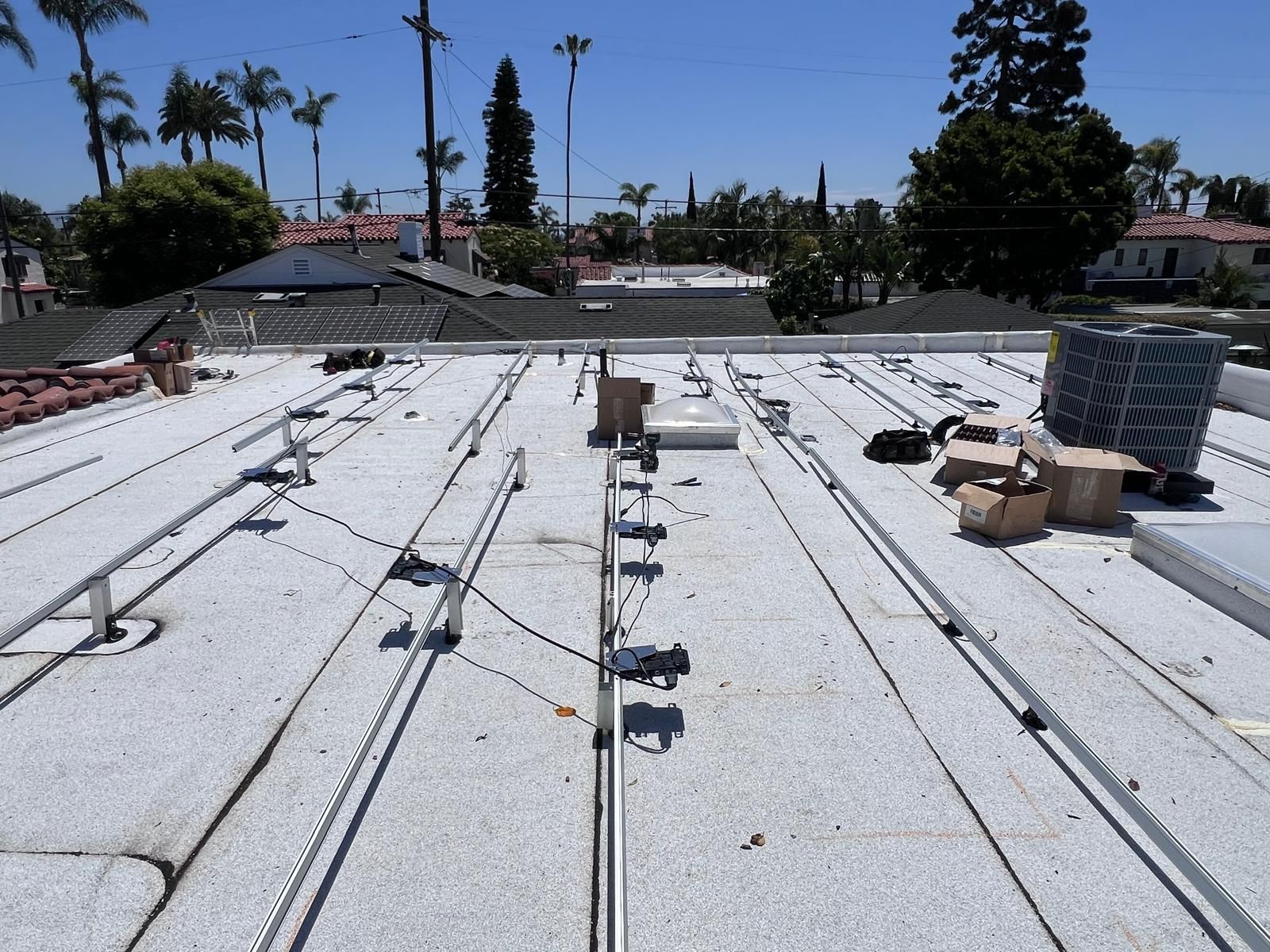 Flat white rooftop with vents, cables, and HVAC equipment under a clear blue sky.