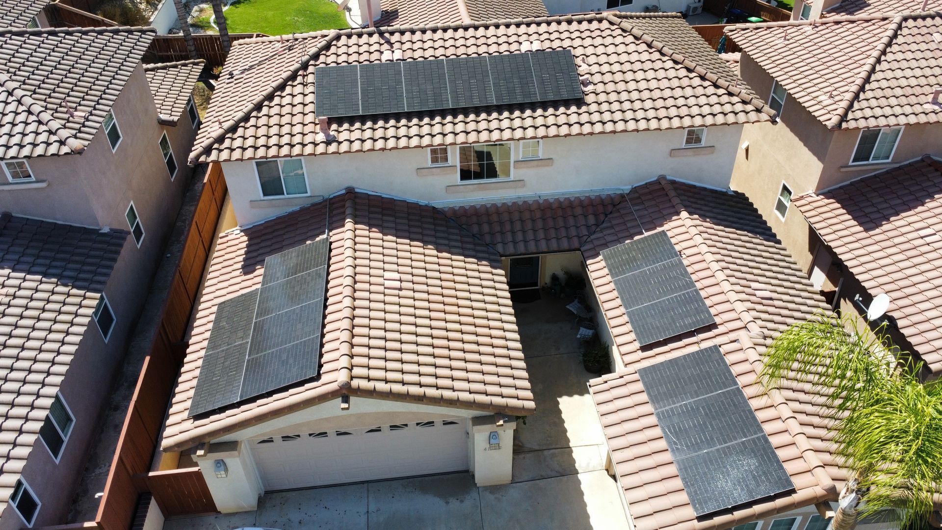 Aerial view of suburban houses with tiled roofs and solar panels on several rooftops.