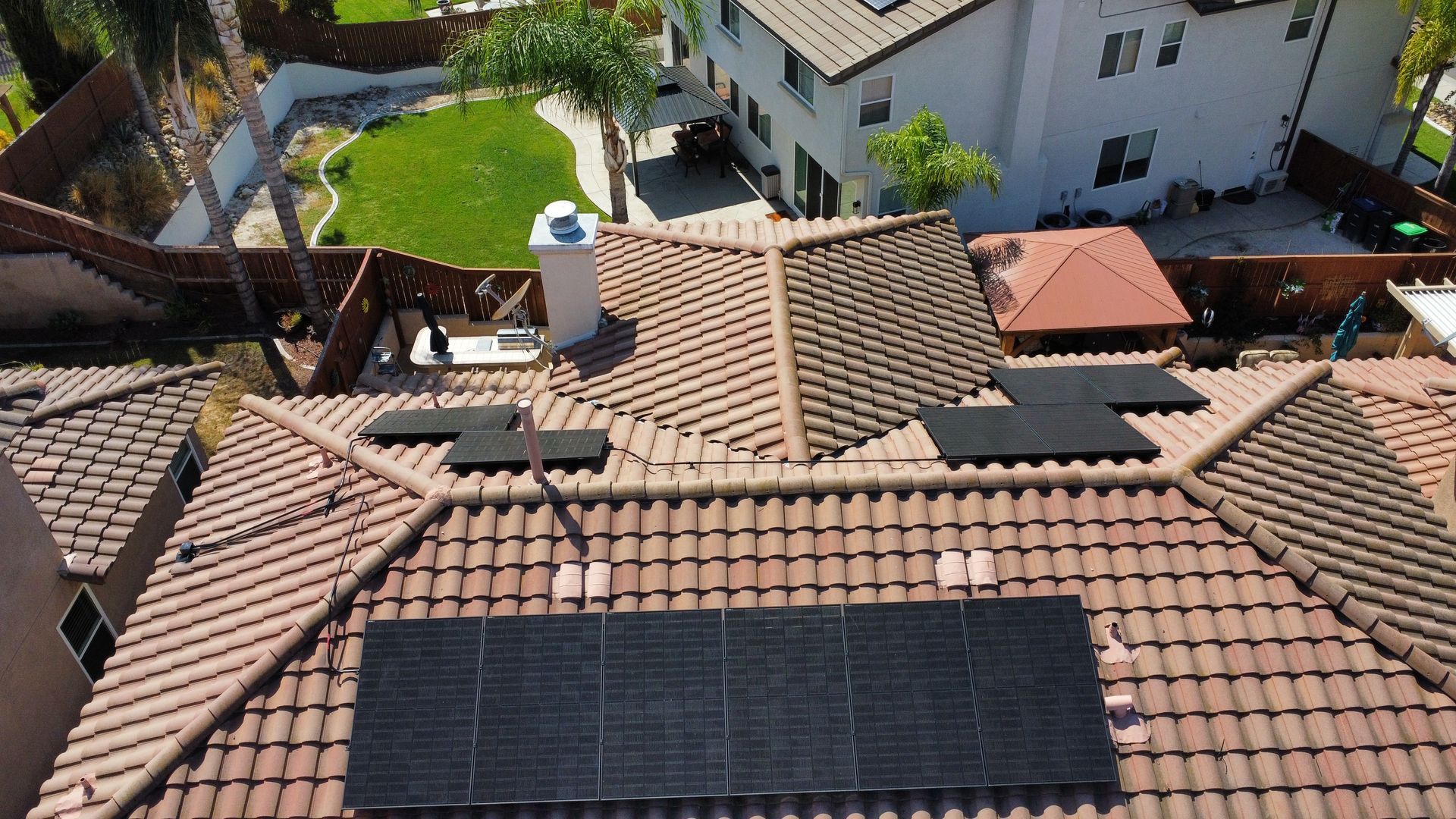 Solar panels on a red-tiled roof in a suburban neighborhood, viewed from above