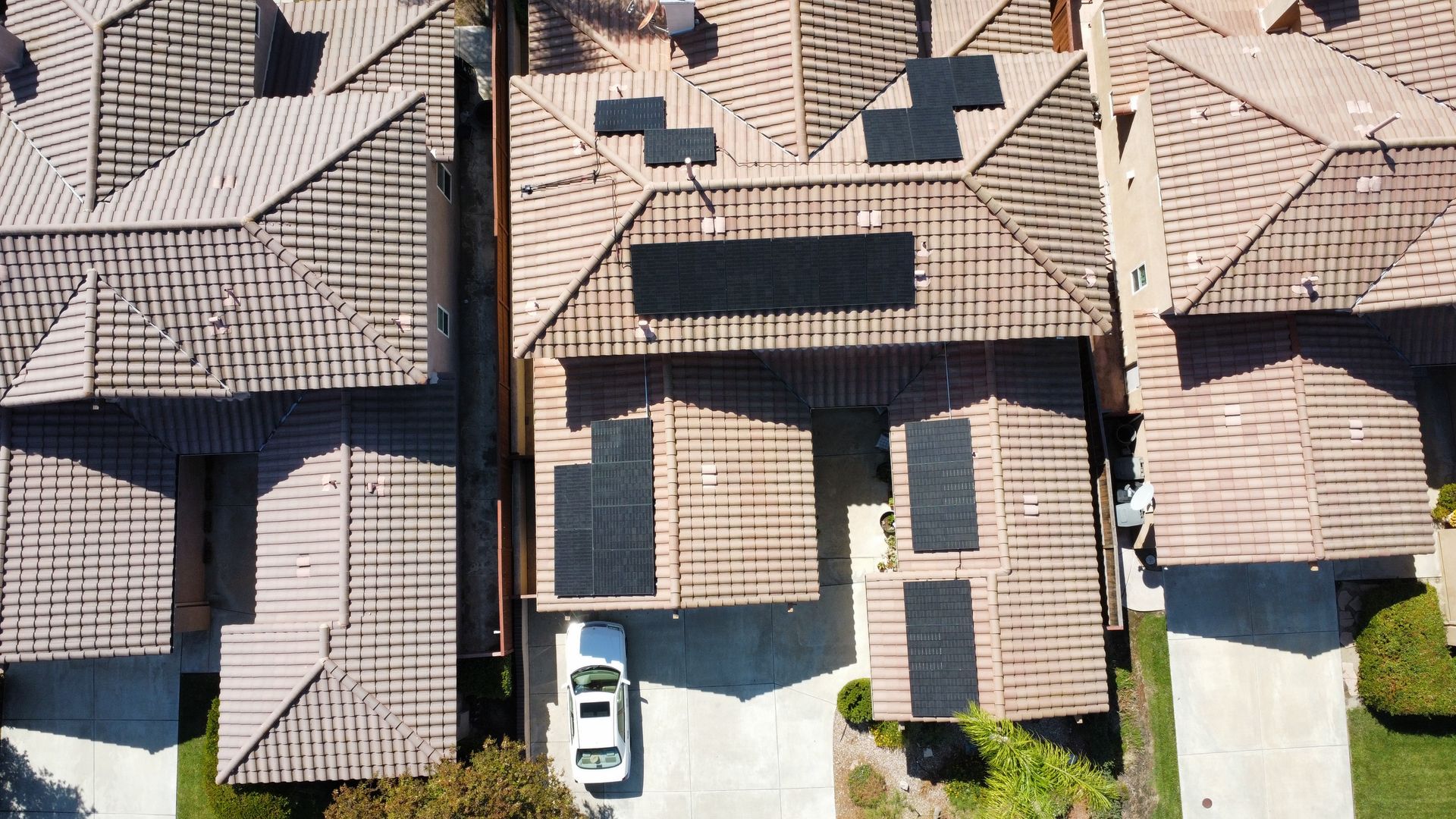 Aerial view of several houses with brown tiled roofs, skylights, and small front yards.