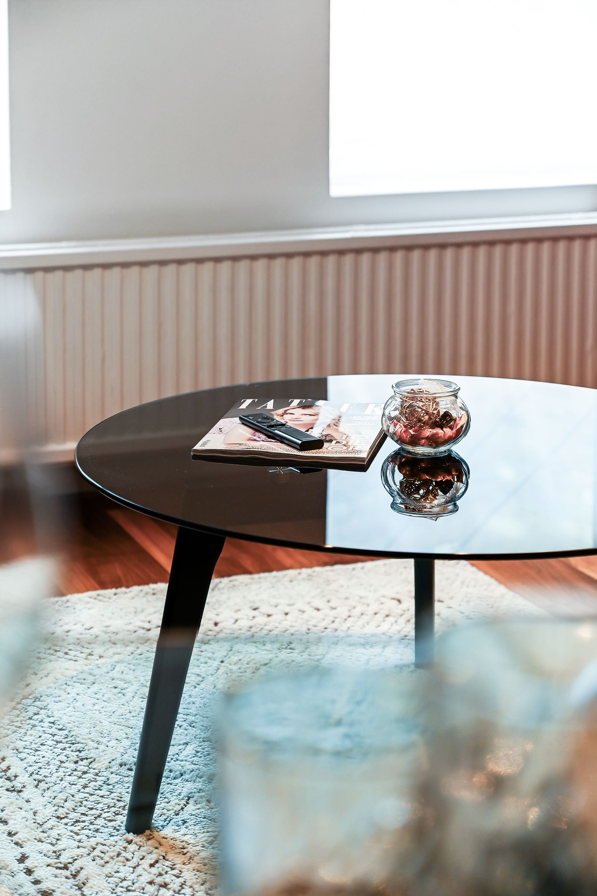 Round black coffee table with a magazine and glass bowl in a bright living room near a window.