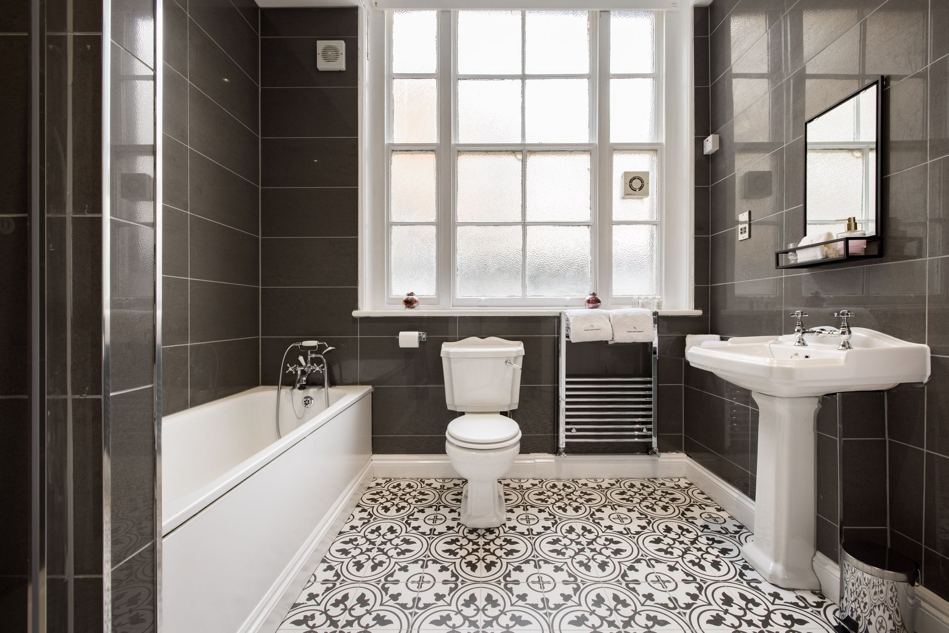 Modern bathroom with bathtub, toilet, pedestal sink, patterned tile floor, and large window